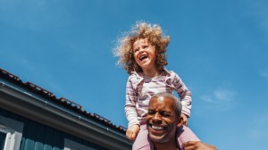 En liten jente sitter på skuldrene til pappaen sin. De har det gøy og smiler.