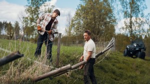 Mann i rutete skjorte står inne i en låve med synlige bjelker og trepaneler i bakgrunnen.