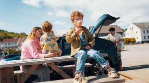 Familie tar en pause ved bilen – barn spiser is, mens en voksen pakker ut fra bagasjerommet.
