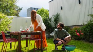 Kvinna och man dukar och grillar i sin trädgård