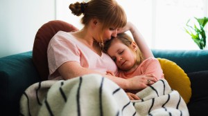 Mamma och dotter som kramas under en filt i soffan