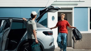 To personer pakker bagasje i en bil utenfor et hus, klare for å dra av gårde.