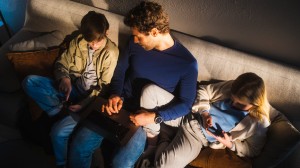 En pappa och två barn som sitter i en soffa och tittar på en laptop
