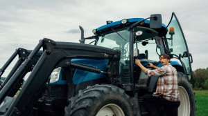 Familie på tre personer som står ved og sitter i en traktor på ett jorde med gult høy 