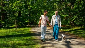 Et kjærestepar leier hender i en park. En av dem holder en hund i bånd.