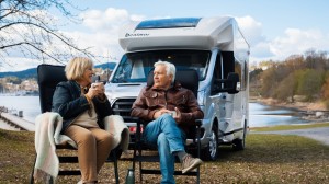 Et eldre par sitter foran bobilen sin og drikker kaffe