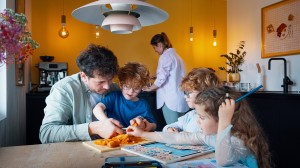 En familie på fire siitter i sofaen og smiler. Barna leker med noen leker.