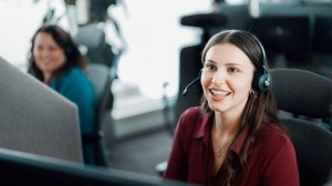 Smilende ung kvinne med øretelefoner sittende bak et skrivebord