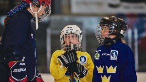 Två barn på en hockeyrink som pratar med en vuxen hockeyspelare