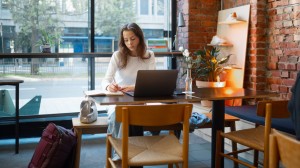 En kvinnelig student sitter på cafe og jobber på PCen sin.