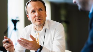 A man in a white shirt is in discussion with a colleague, gesticulating with his hands.