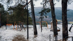 En lekeplass oversvømt av vann, med lekeapparater delvis under vann og trær rundt. 