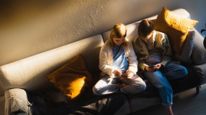 Flicka och pojke som sitter i soffa och kollar på sina mobiler