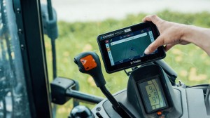 Mann i rød skjorte betjener en skjerm i en traktor med utsikt over et jorde.