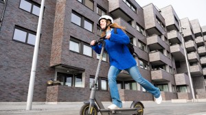 En ung kvinne kjører med elsparkesykkelen sin forbi noen boligblokker.