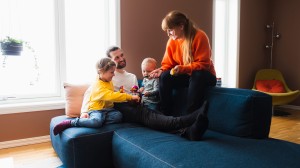 Familie på to voksne og to små barn sitter i sofaen og leker