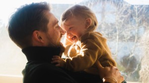 Nærbilde av en smilende far med et smilende barn tatt ved et vindu hvor solen skinner inn
