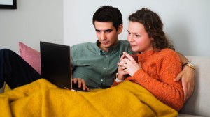 Ungt par tittar på datorn tillsammans i soffa