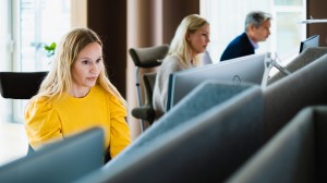 Kvinna i gul tröja vid datorn på ett kontor