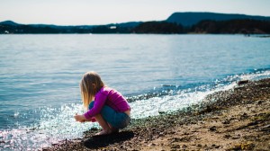 Et barn leker på en strand og sitter på huk ved vannet