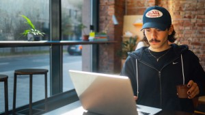 En ung mann sitter på en kafé og ser på en bærbar PC