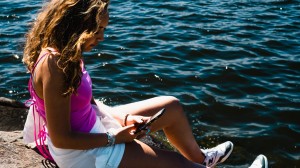 Ung tjej som sitter med sin mobil på en klippa vid havet
