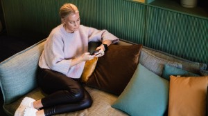 En kvinne sitter i en sofa og ser på mobilen sin
