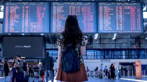 Kvinna med ryggsäck och kaffe i handel tittar på avgångstavla på flygplats