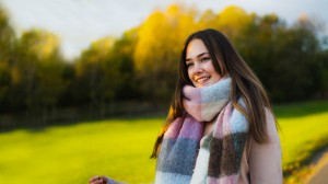 Jente med stort skjerf står i parken og smiler