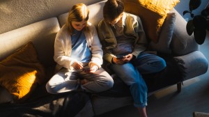 Jente og gutt sitter i sofaen og ser på hver sin mobiltelefon.