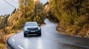 En bil kjører på en landevei, med skog i høstens farger i bakgrunnen.